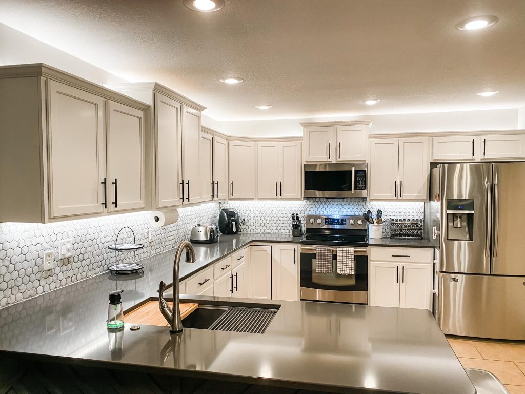 Background image of remodeled kitchen, white cabinets, tile backsplash, and stainless appliances